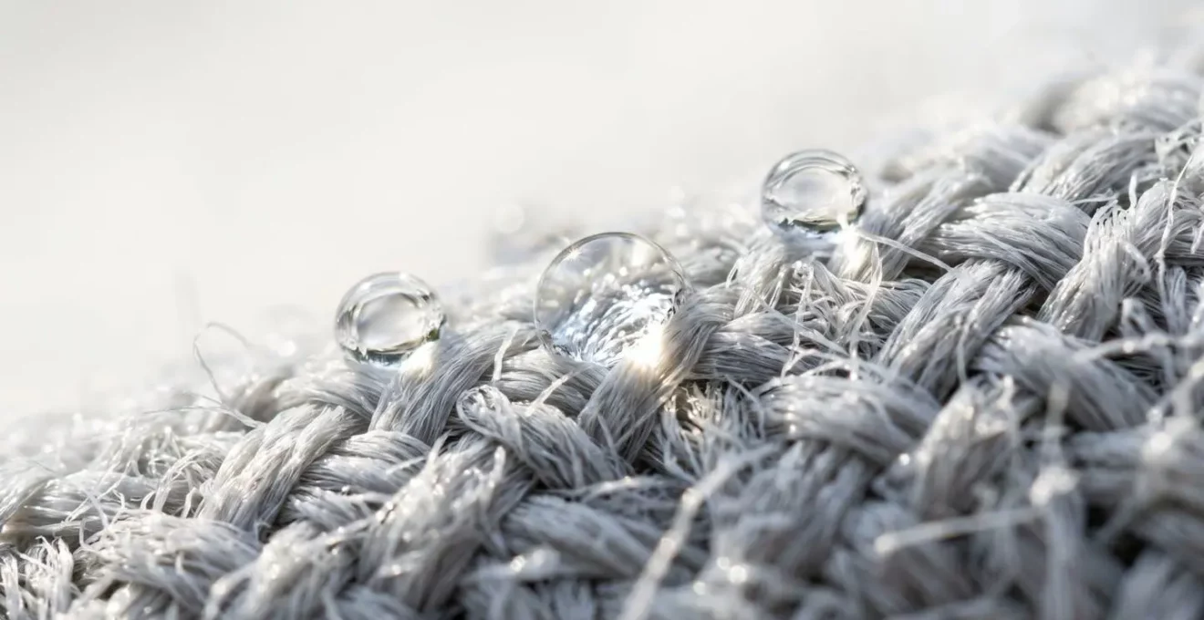 Gros plan extrême sur une fibre textile technique super absorbante avec gouttes d'eau visibles en surface, texture macro détaillée, fond flouté blanc propre